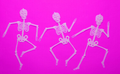 Halloween background. Dancing skeletons on purple background. Top view