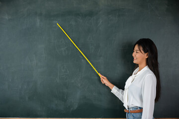 Back to school concept. Happy beautiful young woman standing hold pointer to back board, Asian female teacher smiling with wooden stick pointing to blackboard at school in classroom, Education