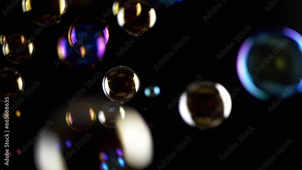 Poster Colorful Soap Bubbles Fly in Empty Space on Isolated Black Background. Colorful lights. Many rainbow transparent bubbles randomly rotate, float, fall, burst. Blurred motion. Selective focus. Abstract.
