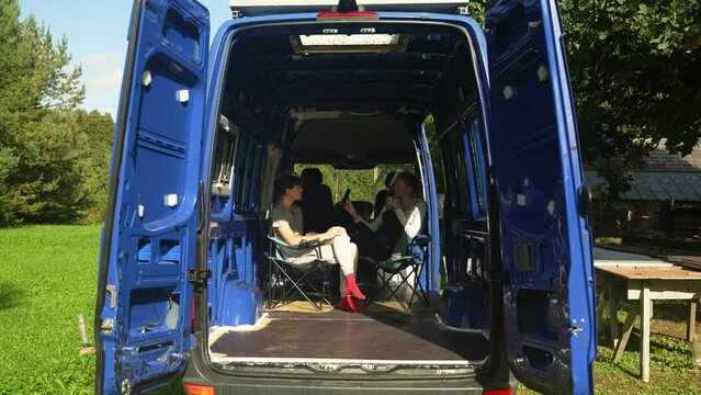 Young couple sits in their van and drinks morning coffee. Man and woman discuses about their project and upcoming tasks in the van build.
