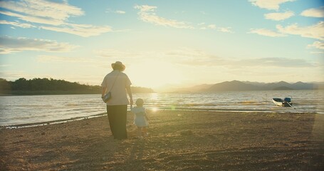 happy Asian Family Love mother holding Daughter hand and walking on the beach during Golden Hour...