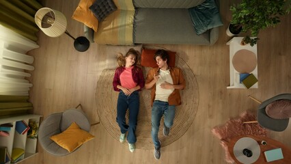 Top view capturing a young couple laying on the floor next to each other, talking to each other and...