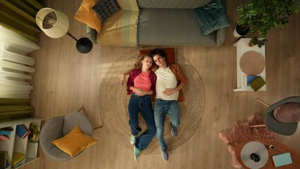 Top view capturing a young couple laying on the floor together, cuddling, hugging, talking to each other warmly and laughing.