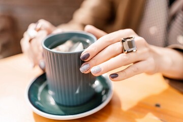 woman holding a cup of hot cappuccino coffee in a cafe on the street, rings on her fingers.