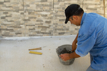 Image of a bricklayer mixing cement and glue in a bucket. Manual work of masonry and tiling.