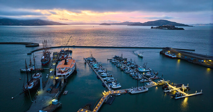 Sunset lighting over San Francisco Bay with Alcatraz and Hyde St Pier lit up at night aerial