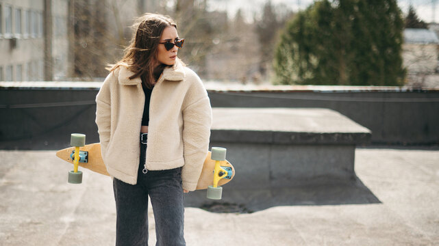 Beautiful woman with skateboard standing on building rooftop