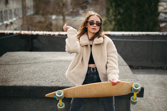Pretty woman sitting with skateboard on sunlight rooftop