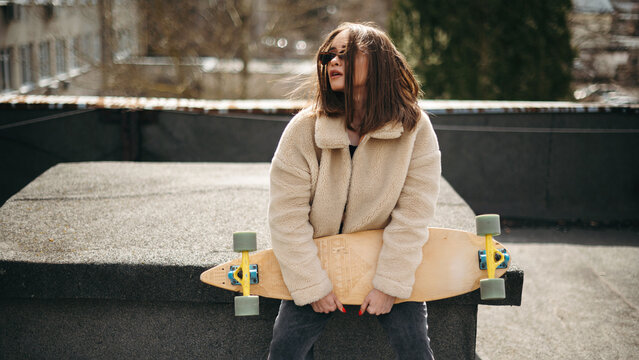 Pretty woman sitting with skateboard on sunlight rooftop