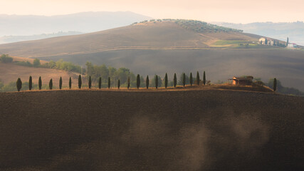 Morning mist through the valley of Val d'Orcia in the scenic countryside farmland and rolling hills of rural Tuscany, Italy.