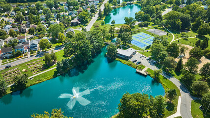 Aerial over Lakeside Pond with fountain near playground and tennis courts in neighborhood