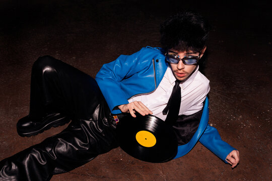 Retro-styled man lounging with vinyl record in the dark