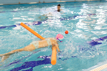 Preschooler girl practices swimming with instructor's supervision