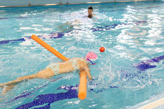Preschooler girl practices swimming with instructor's supervision
