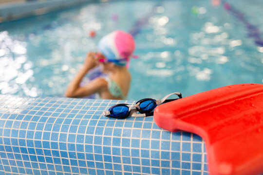 Child swimmer prepares beside pool with kickboard and goggles