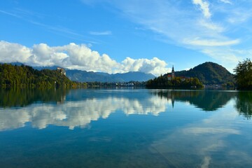 Naklejka premium View of Bled lake and town with the church on an island and a reflection of the clouds in the water