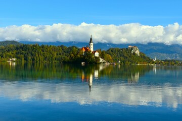 View of Bled lake and the church of the Assumption of Mary on the island and Bled castle behind with clouds covering the mountains in Gorenjska, Slovenia