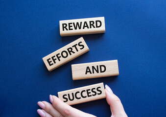 Reward Efforts and Success symbol. Concept words Reward Efforts and Success on wooden blocks. Beautiful deep blue background. Businessman hand. Business concept. Copy space.