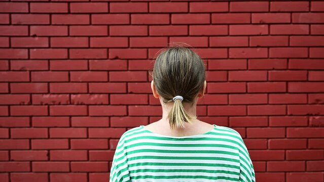 Dead end concept, rear view of casual brunette female facing the red brick wall