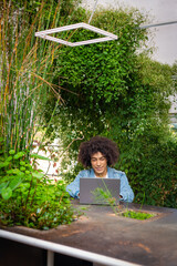 Smiling young ethnic guy ,dressed in casual clothes, works on a laptop outdoors, in a green area in nature. Green open space for coworking, freelancer, relaxing, coffee, food. Free place to work