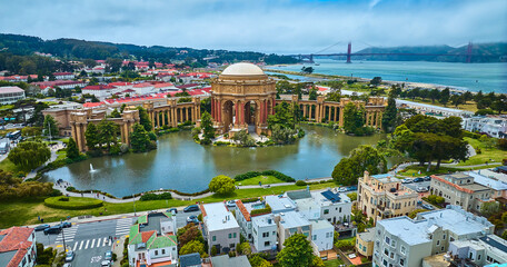 Palace of Fine Arts colonnade and open rotunda on pond with city and Golden Gate Bridge aerial