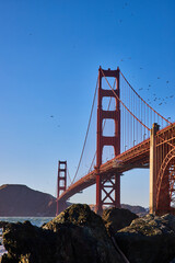 Large rocks with Golden Gate Bridge looming above and distant mountainous shoreline