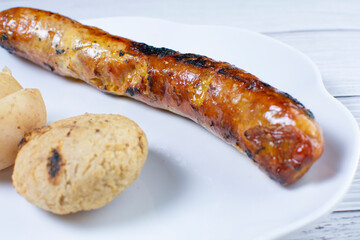 fried chorizo, potato flared and arepa on a white plate and light wooden background