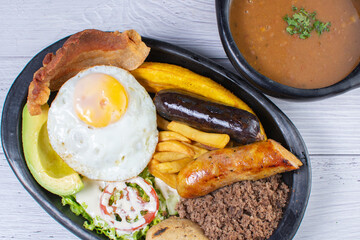 Typical Colombian dish, tray paisa, plate of beans, ground meat, arepa, fried egg, chicharron, French fries, chorizo, salad, ripe plantain and avocado