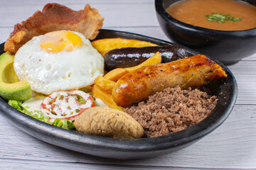 Typical Colombian dish, tray paisa, plate of beans, ground meat, arepa, fried egg, chicharron, French fries, chorizo, salad, ripe plantain and avocado