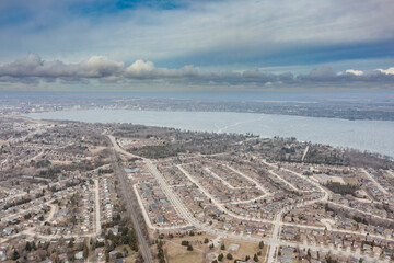 : Aerial view of Barrie, Ontario, showcasing a frozen Lake Simcoe on a cloudy day. Residential areas line the icy lake, reflecting the serene winter landscape of Canada.