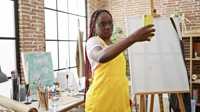 Confident african american woman artist smiling as she boldly makes a selfie with her smartphone at her inspiring art studio