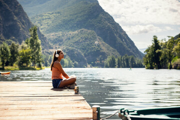 Beautiful woman listening to music with headphones while relaxing sitting by a lake