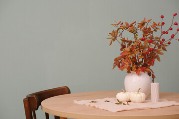 Autumn home interiors, ceramic vase with red leaves, candle, two pumpkins on round wooden table.
