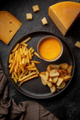 Fried potatoes, fries with cheese sauce on a black plate, dark table..Beer snacks, potato snacks in assortment Beer snacks, potato snacks in assortment