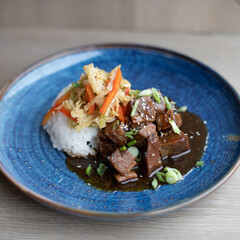 Sous Vide Braised Beef with Rice and Slaw on a Dark Blue Plate