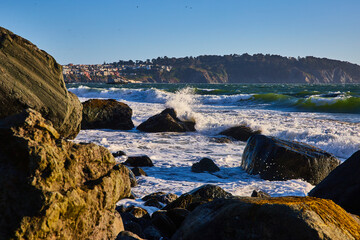 Big waves rolling into massive boulders with ocean spray around partially submerged rock