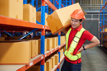 factory worker holding corrugated boxes and suffering back pain beside shelf in the warehouse...