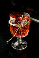 Beautiful view of glass with red alcoholic cocktail decorated with twig of gypsophila standing on the bar