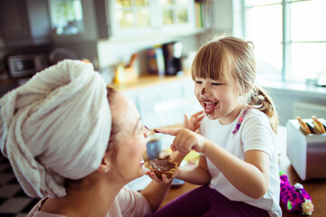 Happy young girl daubing her mother with chocolate spread in the kitchen