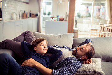 Loving young father lounging on the couch with his son at home