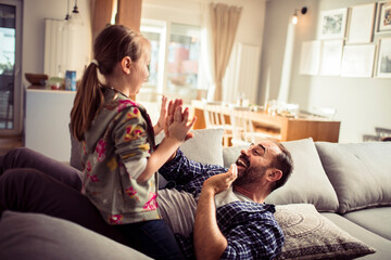 Happy young father playing patty cake with his daughter on the couch at home