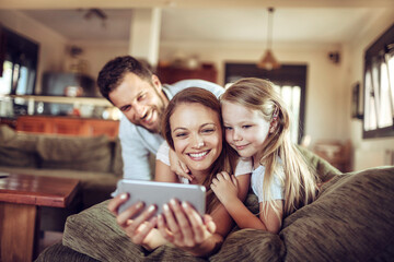 Happy young family looking at the smartphone on the couch at home