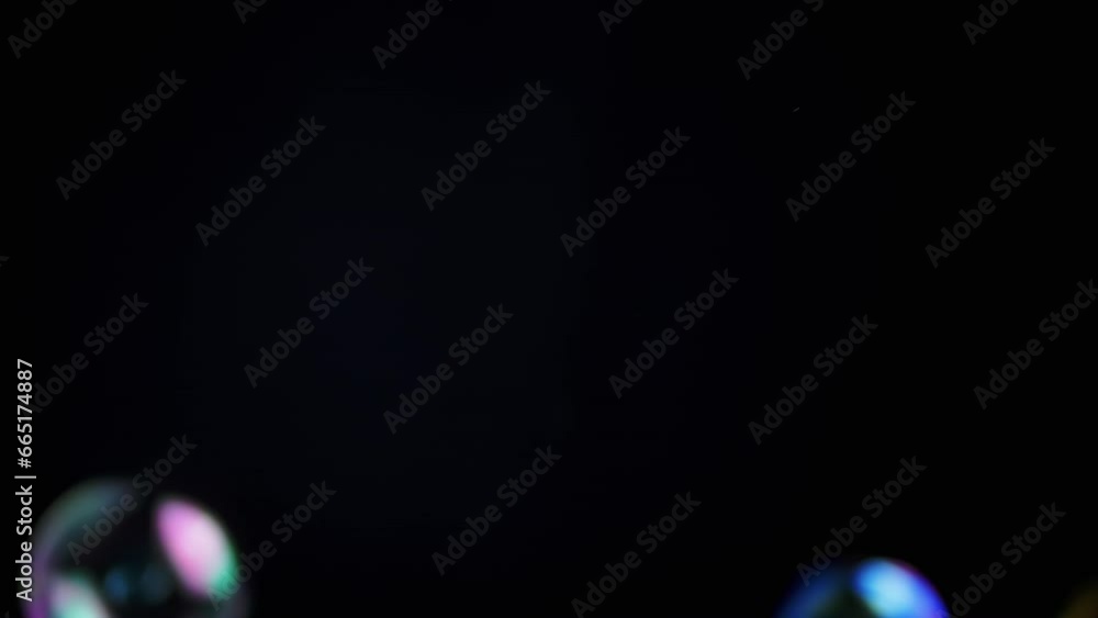 Poster colorful soap bubbles fly in an empty space on isolated black background. many large, small rainbow 