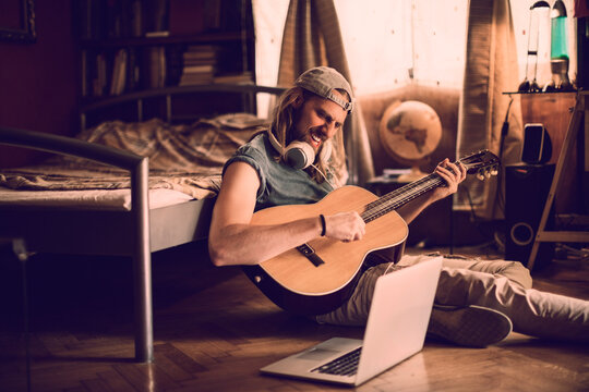 Young musician playing the guitar on the bedroom floor at home