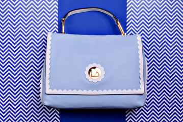 Stylish women's top-handle bag in blue leather with decorative wavy trim and gold hardware on a...