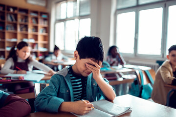 Stressed young boy doing a test in a elementary school classroom