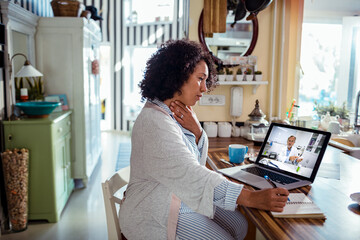 Middle aged woman writing down recommendations from her doctor during online medical consultation