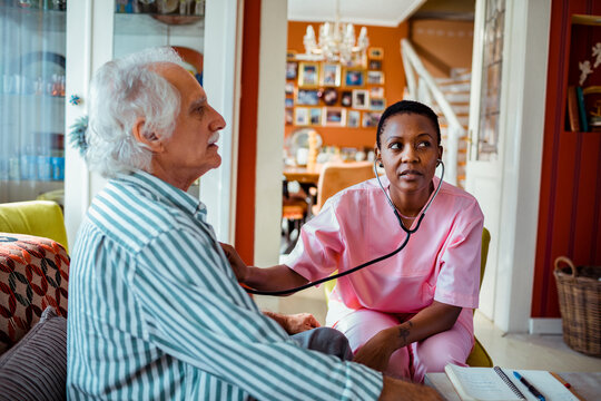 Young female caregiver examining a senior patient at home