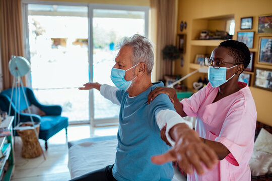 Young African American Female Caregiver Helping Her Senior Patient Stretch At Home