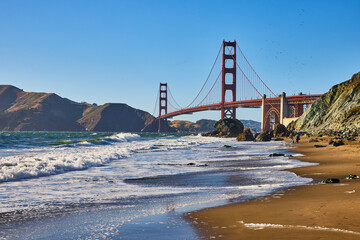 Sandy beach with people walking along surf toward Golden Gate Bridge